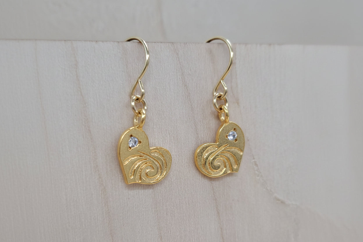 Gold heart-shaped earrings with intricate designs on a light wooden surface.
