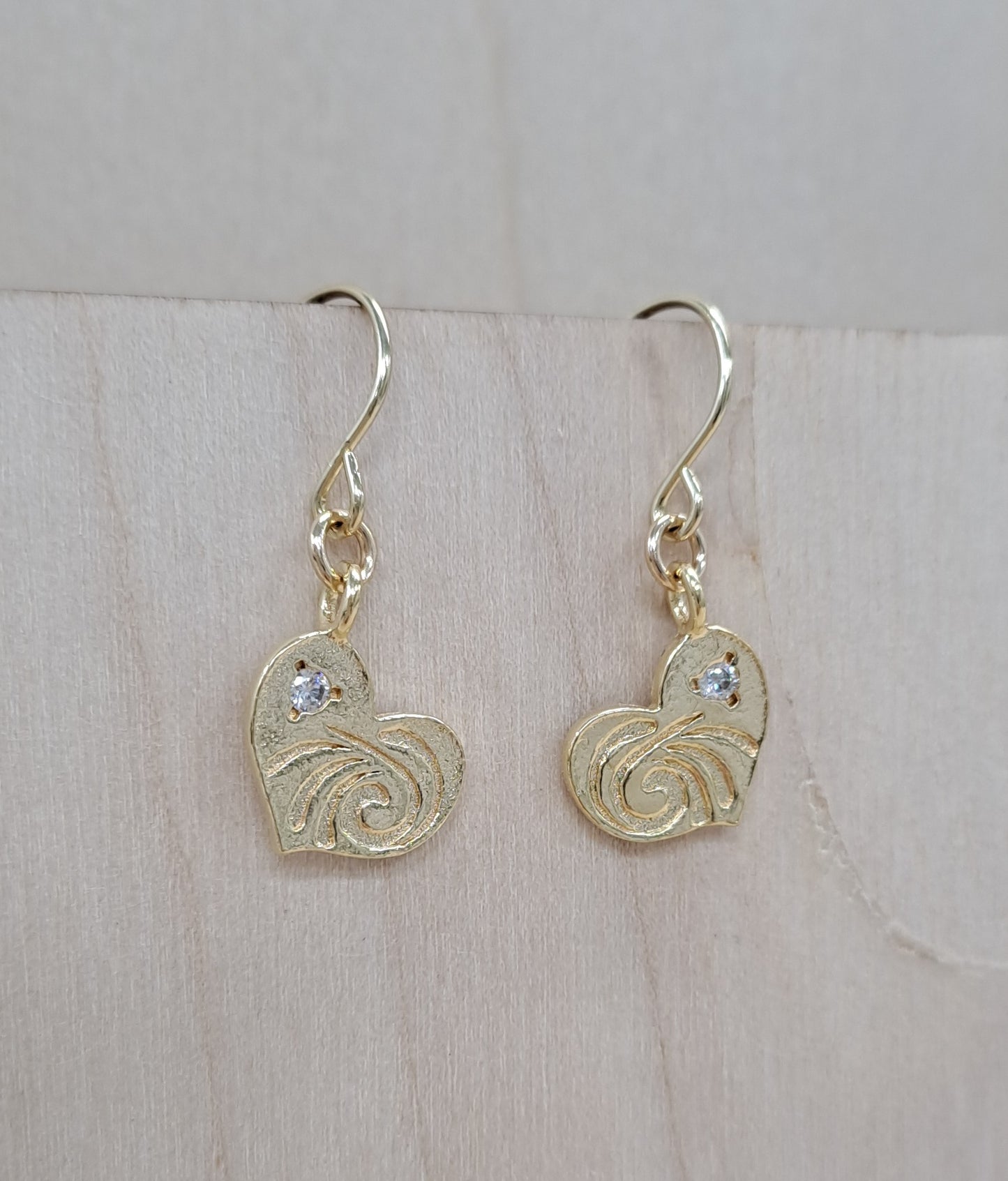 Gold heart-shaped earrings with intricate designs on a light wooden surface.