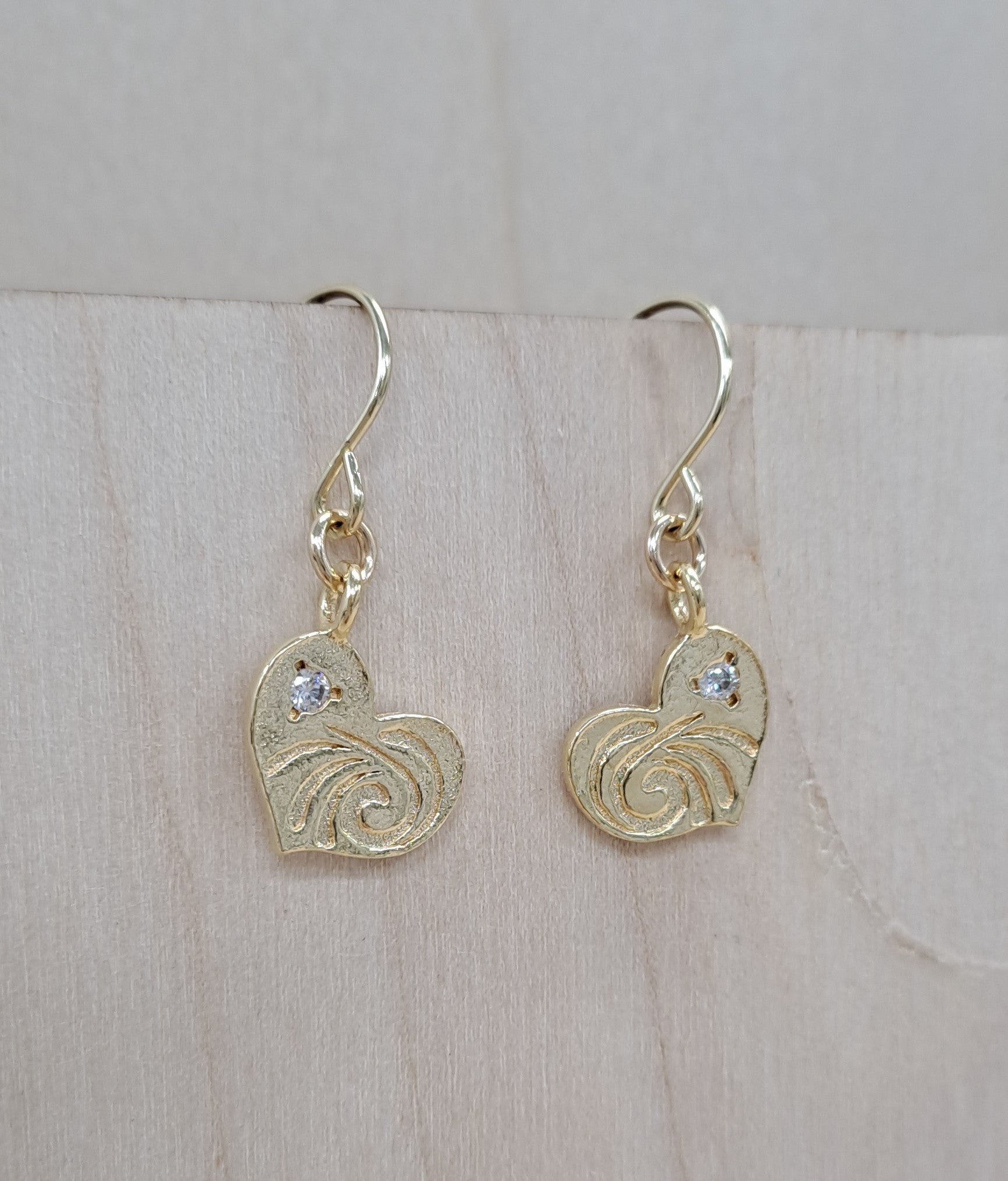 Gold heart-shaped earrings with intricate designs on a light wooden surface.